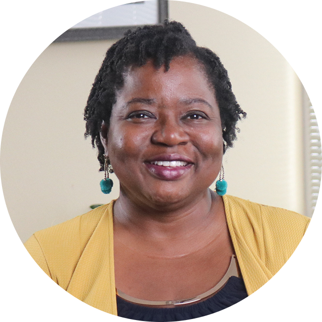 A smiling Black woman named Vernelia with green earrings wearing a yellow cardigan over her black top.