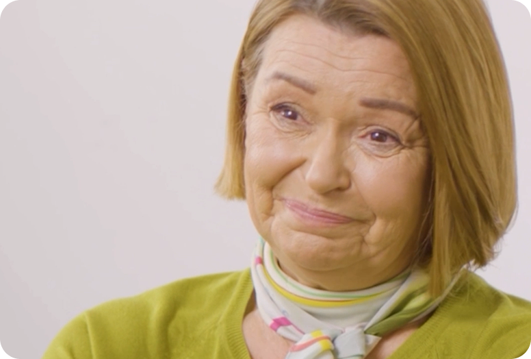 A link to a video. Małgorzata, is an older white woman wearing a lime green cardigan. She is smiling.