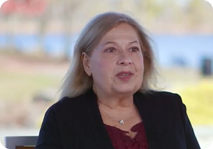 This is a link to a video. Cindy, the subject, is wearing a black blazer over a red top, and has shoulder-length straight blonde hair.