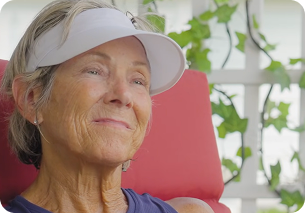 This is a link to a video. Karin, a person living with multiple myeloma. She is wearing a white visor and a blue tank top, and is sitting in a red chair.
