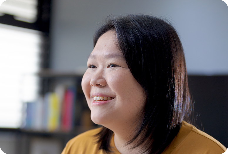 An Asian woman named Andrea with shoulder-length hair and wearing a yellow top. She is smiling and looking off to the left