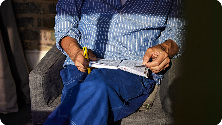 A person writing notes with a yellow pen into a notebook. They are wearing a blue shirt and blue denim jeans.