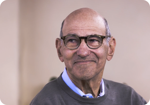 A link to a video. An older man with a grey shirt, smiling and looking left.
