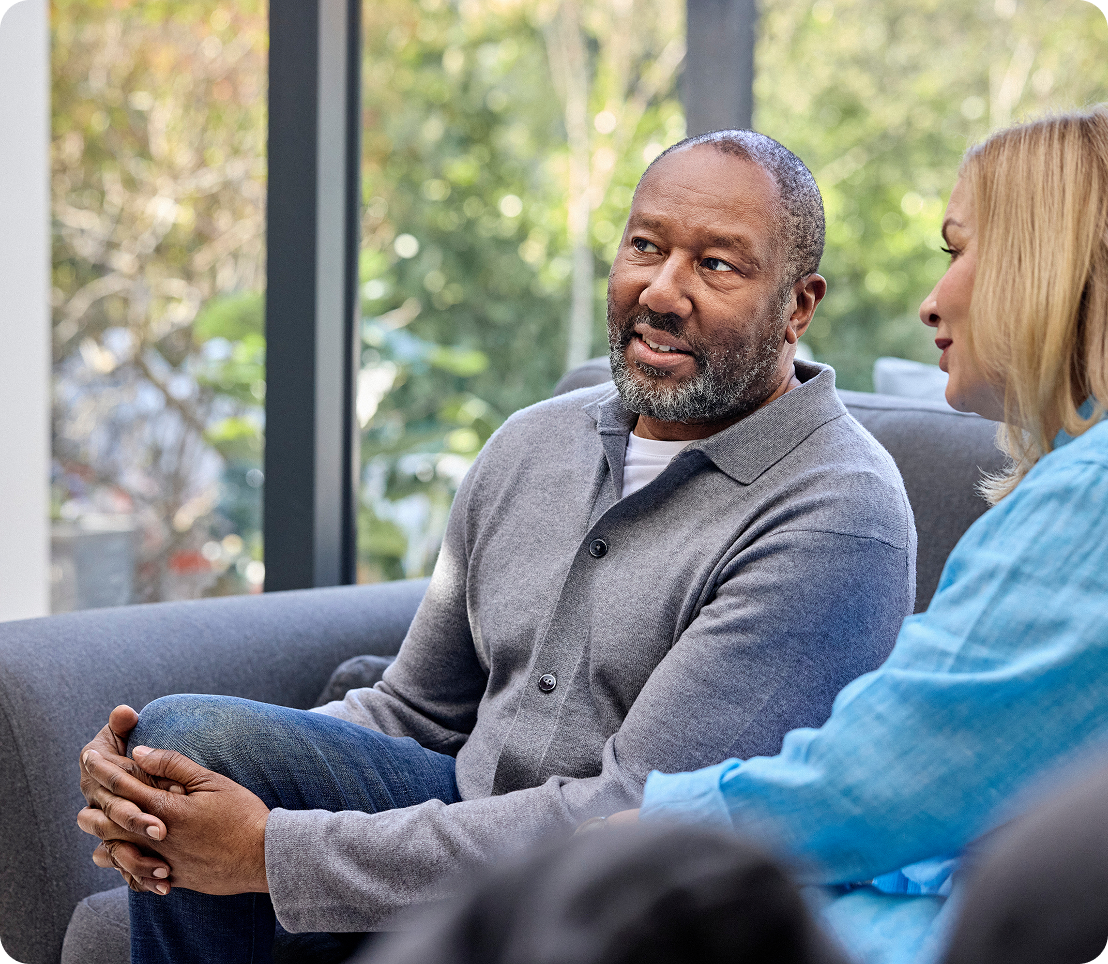 An older black man with a bear speaking with a younger woman with blond hair.