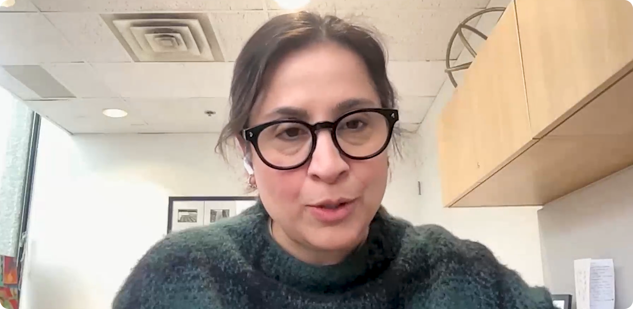 A link to a video. Dr. Ahmed is speaking. She is wearing black glasses and a forest green sweater.