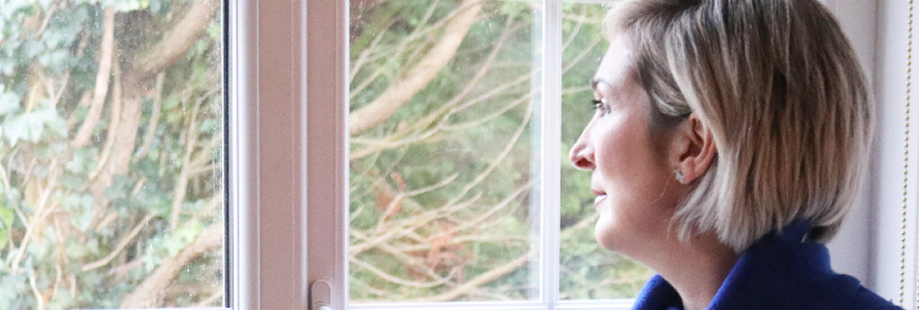 Lou, a woman with short blonde hair facing left, looking thoughtfully out a window.