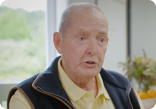 A link to a podcast. An older man wearing a blue vest and a yellow shirt, talking to an interviewer off to the right.