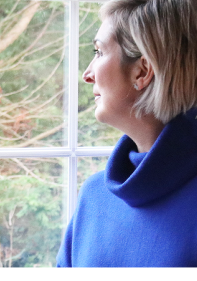 Lou, a woman with short blonde hair facing left, looking thoughtfully out a window.